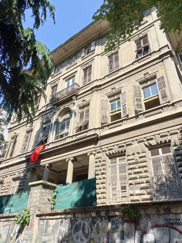 Sarıca Arif Paşa Konağı'nın cephesine aşağıdan bakış; süslü pencere sövesi, balkonlar, ağaçlar ve alt kattaki duvar yazıları.