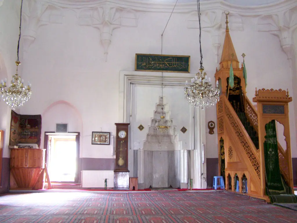 Rum Mehmed Paşa Camii'nde mihrap ve minber; beyaz mukarnaslı mihrap nişi, ahşap minber, avizeler ve kırmızı halı.