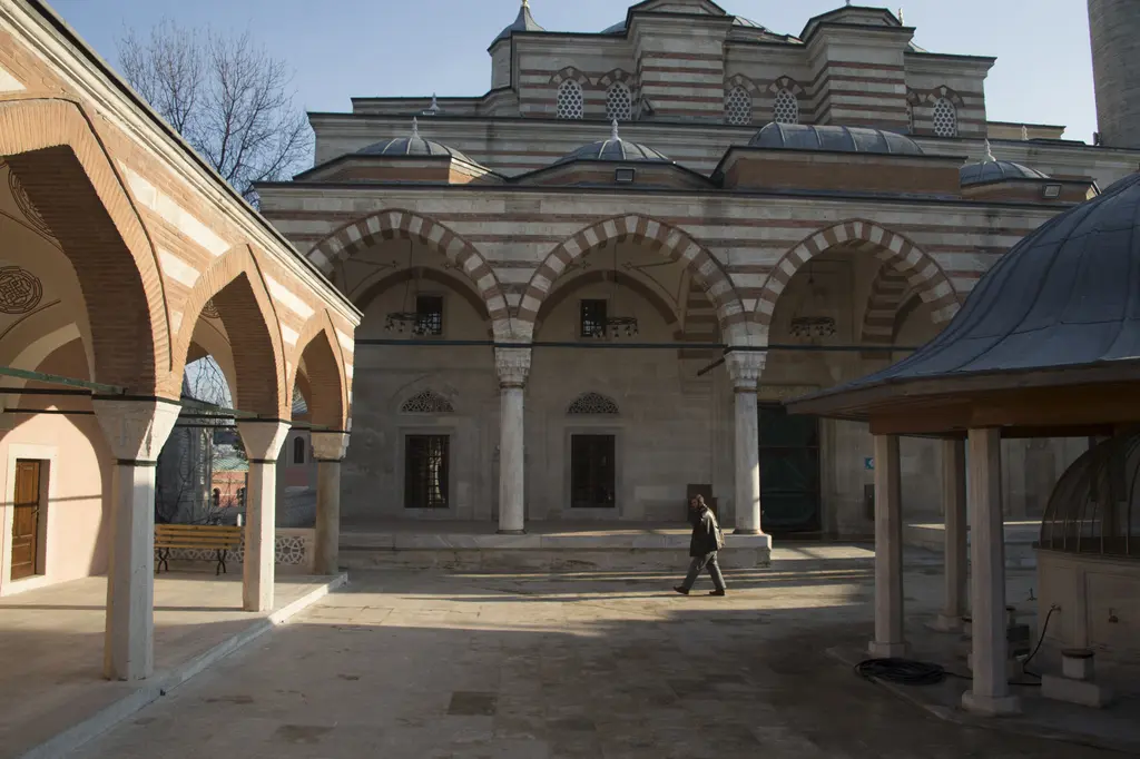 Zal Mahmud Paşa Camii'nin avlusu; medrese revağının kemerleri, karşıda sıralı kemerli son cemaat yeri ve yürüyen bir ziyaretçi.