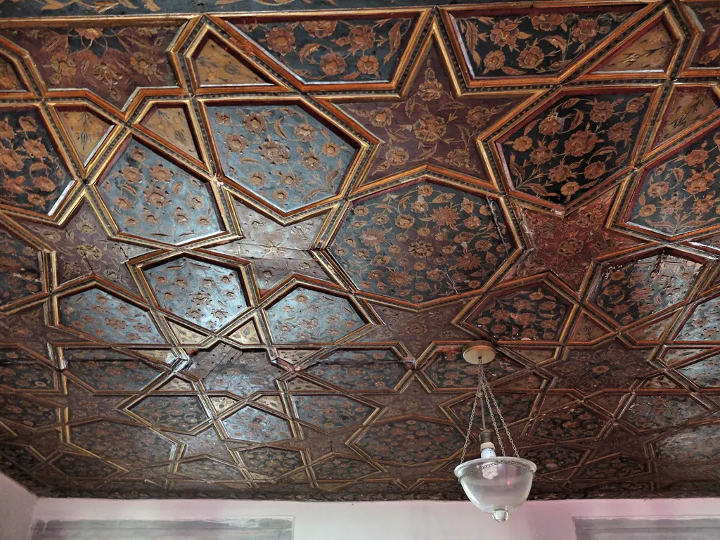 Atik Valide Camii'nde mahfil tavanı; koyu ahşap üzerinde yıldız geçmeli geometrik desen ve sarkan kandil.