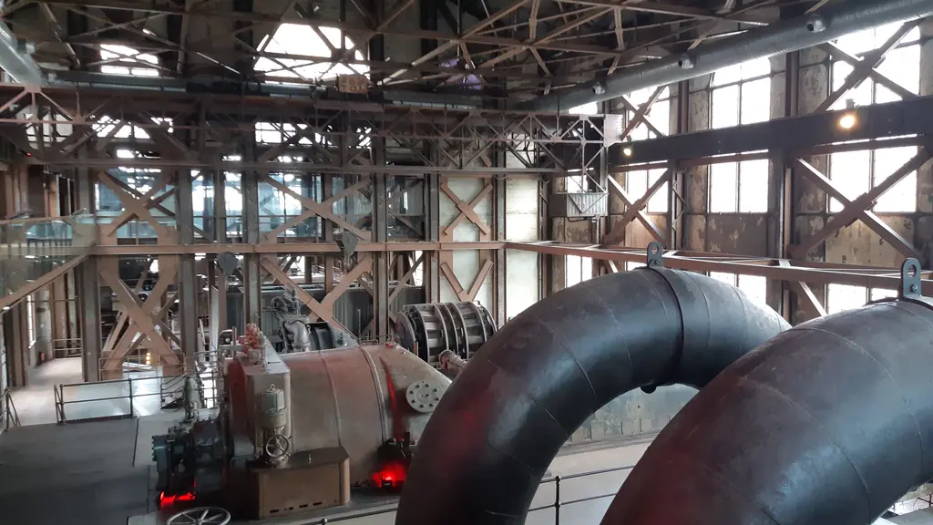 Enerji Müzesi'nde türbin grubu; kıvrılarak inen kırmızı ve siyah kalın borular, arkada makineler ve kafesli pencereler.