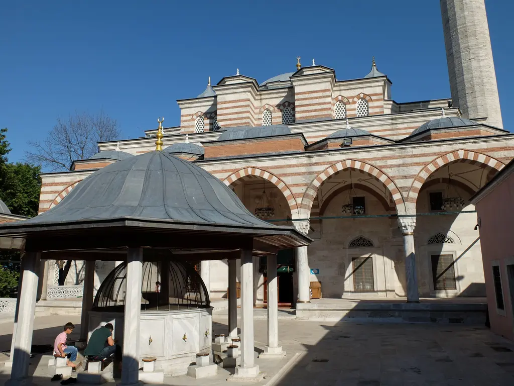 Zal Mahmud Paşa Camii'nin avlusu; kurşun kubbeli şadırvan, kemerli revaklar, taş-tuğla cephe ve ziyaretçiler.