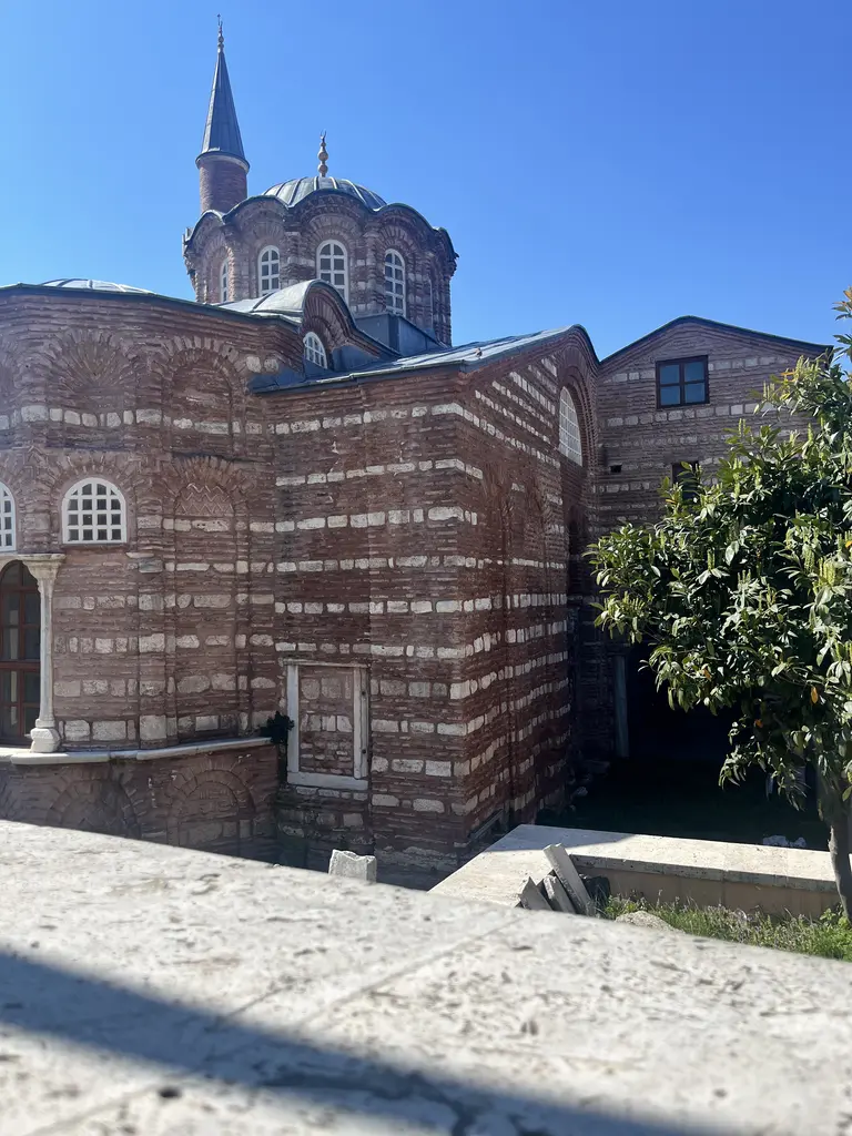 Vefa Kilise Camii'nin doğu ucu beton bir terastan; solda eğrisel apsis duvarı ve kemerli pencere, arkada üç kemerli pencereli kubbe kasnağı ile minarenin gri külahı.