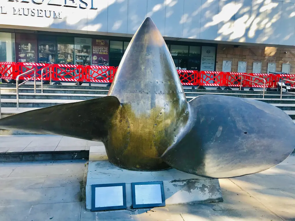 İstanbul Deniz Müzesi önünde büyük bir gemi pervanesi; parlak metal kanatlar, alçak kaide ve önünde bilgi levhaları.