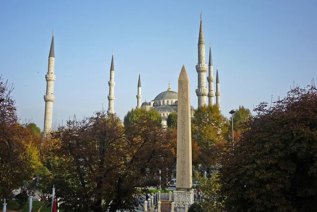 Sonbaharda Dikilitaş; sarı ve kızıl yapraklı ağaçların arasında granit gövde, arkada Sultanahmet Camii'nin kubbeleri ve minareleri.