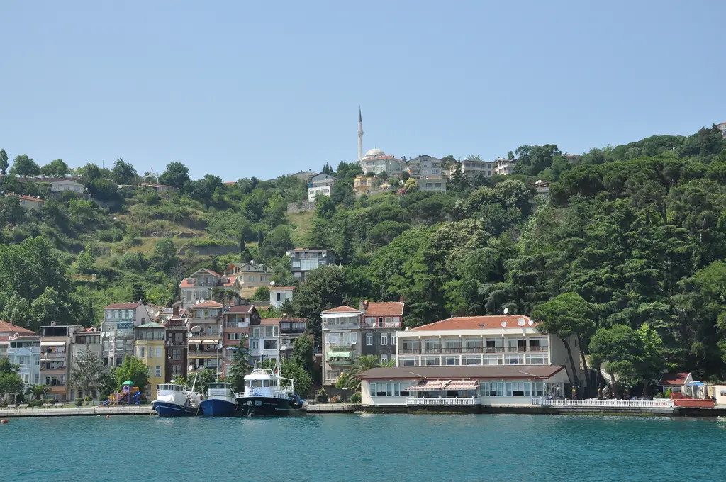Denizden Sarıyer; kıyıda bağlı balıkçı tekneleri, yamaca tırmanan evler, arkada yeşil vadi ve minare.
