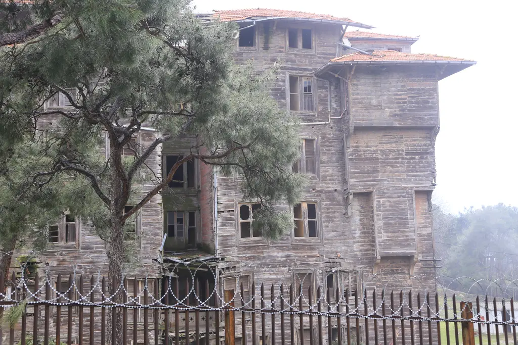 Büyükada Rum Yetimhanesi; dikenli tel örgülü çitin ardında gri ahşap cephe ve sıra sıra pencereler.