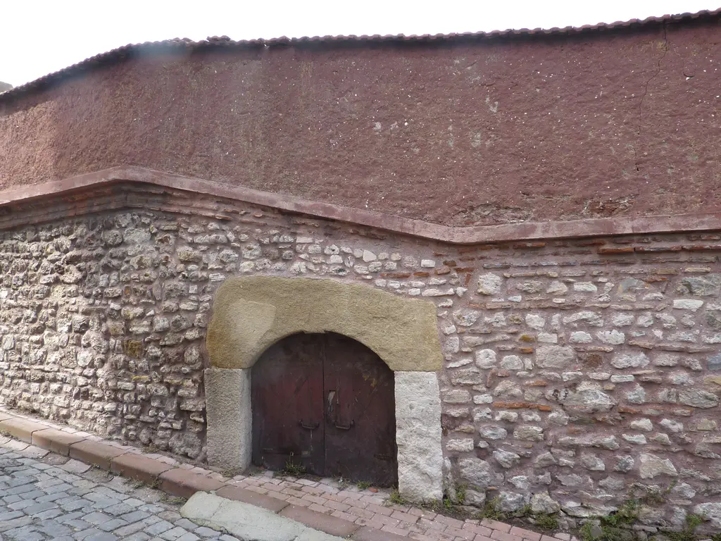 Kanlı Kilise'nin dış duvarında taş söveli kemerli ahşap kapı; moloz taş ve tuğla sıralı duvar, üstünde kırmızı sıva ve arnavut kaldırımı.