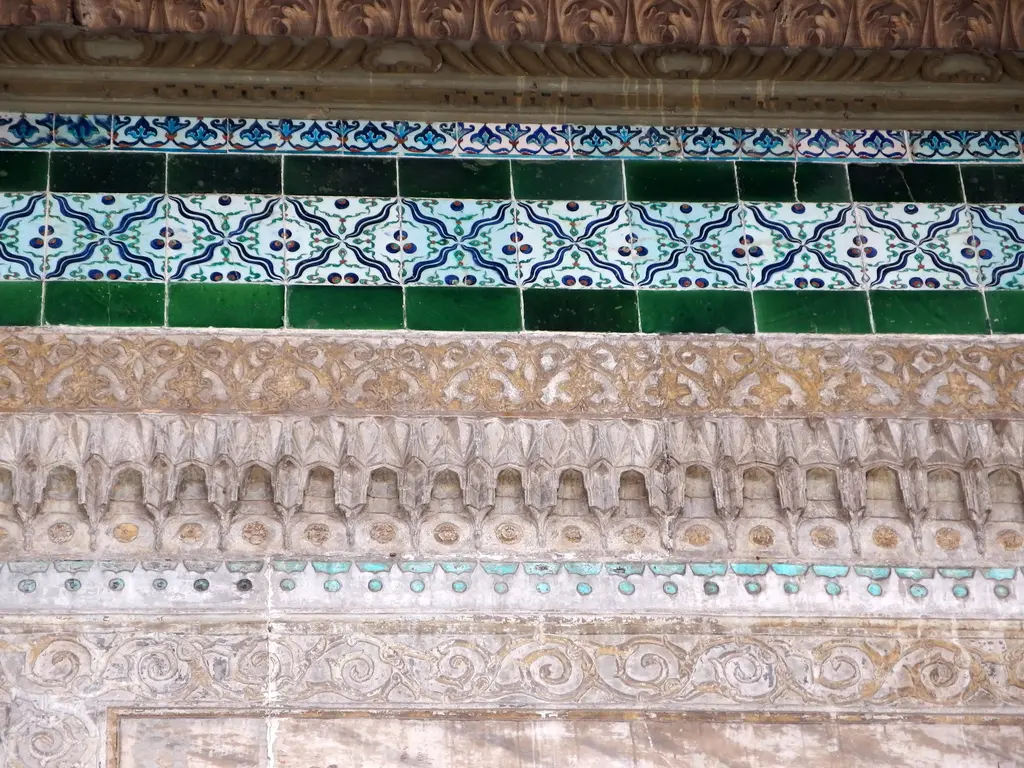 Saçak altındaki bezeme kuşakları; üstte mavi yeşil çini sırası, altında mukarnas dizisi ve kabartmalı mermer friz.
