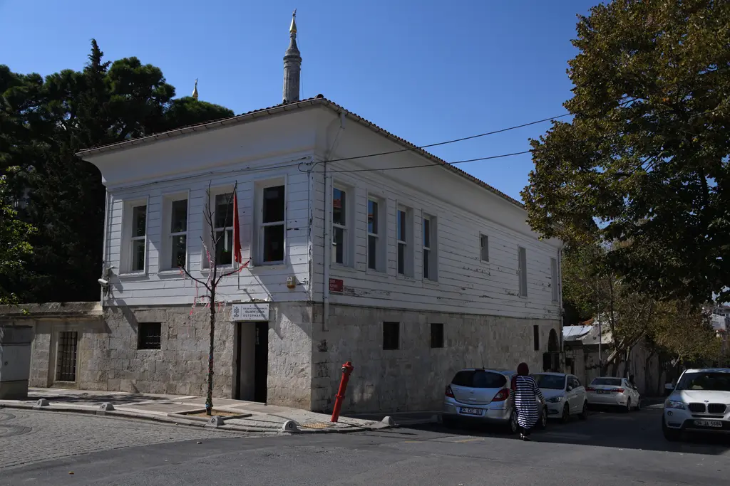 Selimiye Camii'nin sıbyan mektebi; alt katı taş, üst katı beyaz boyalı iki katlı yapı, kiremit çatı ve önünde arabalar.