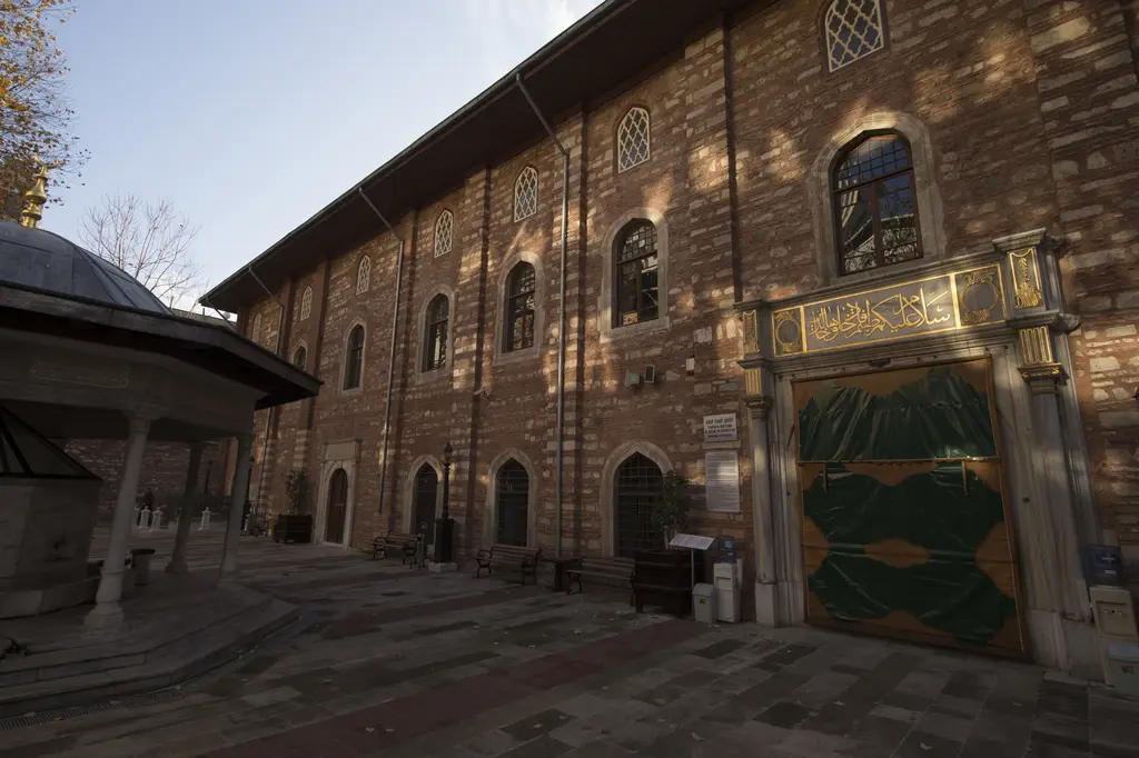 Arap Camii'nin cephesi; kırmızı tuğla ve taş bantlı duvar, sivri kemerli pencereler, yeşil perdeli kapı ve taş avlu.