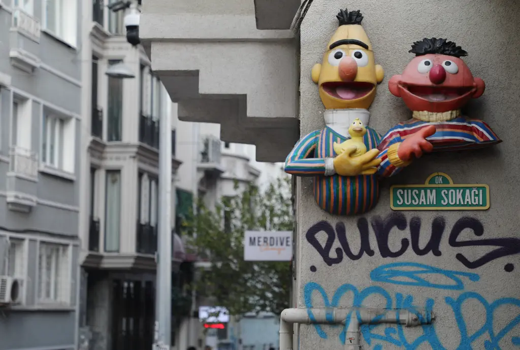 Cihangir'de Susam Sokağı tabelası; yanında iki çocuk dizisi karakteri figürü, alt kısımda grafiti ve arkada apartmanlar.