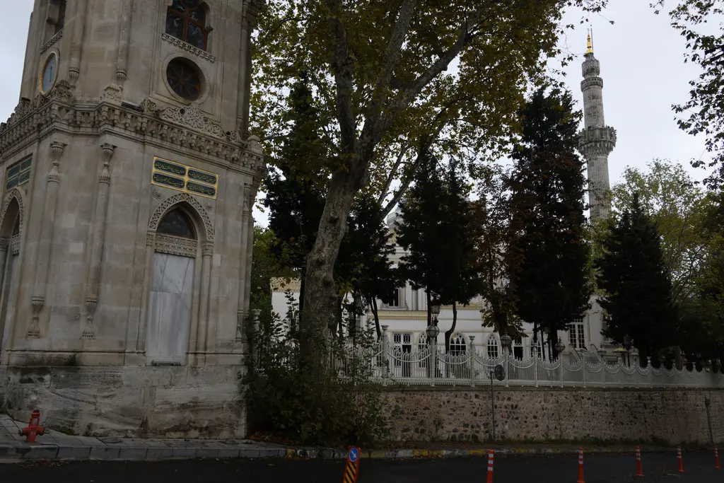 Yıldız saat kulesi ve arkada cami; oymalı taş kule gövdesi, ağaçlar arasında beyaz cephe ve ince minare.