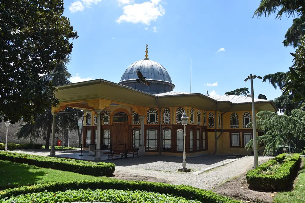 Aynalıkavak Kasrı'nın kara cephesi; tek katlı sarı yapı, önünde sütunlu sundurma, üstünde kurşun kaplı dilimli kubbe ve önde düzenli çit.