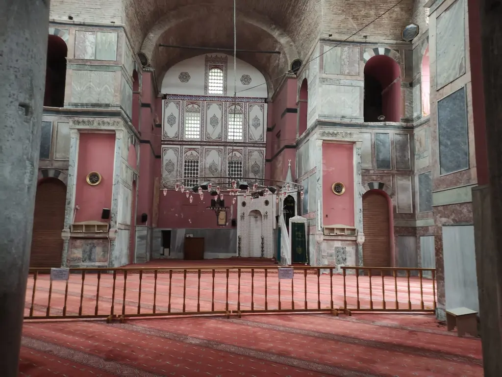 Kalenderhane Camii'nin harimi; kapı eşiğinden mihrap duvarına bakış, önde ahşap bariyer, iki yanda mermer kaplı ayaklar ve hat levhaları.