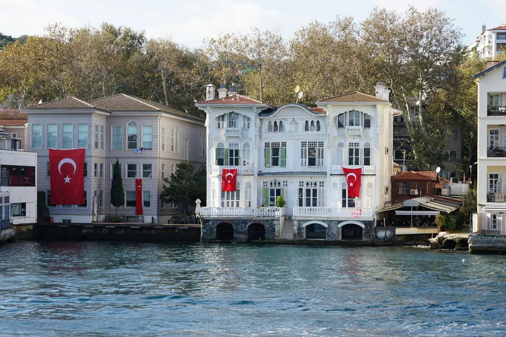 İkiz Yalı; beyaz cephe, kemerli zemin kat açıklıkları, bayraklar ve solda pembe cepheli komşu yalı.
