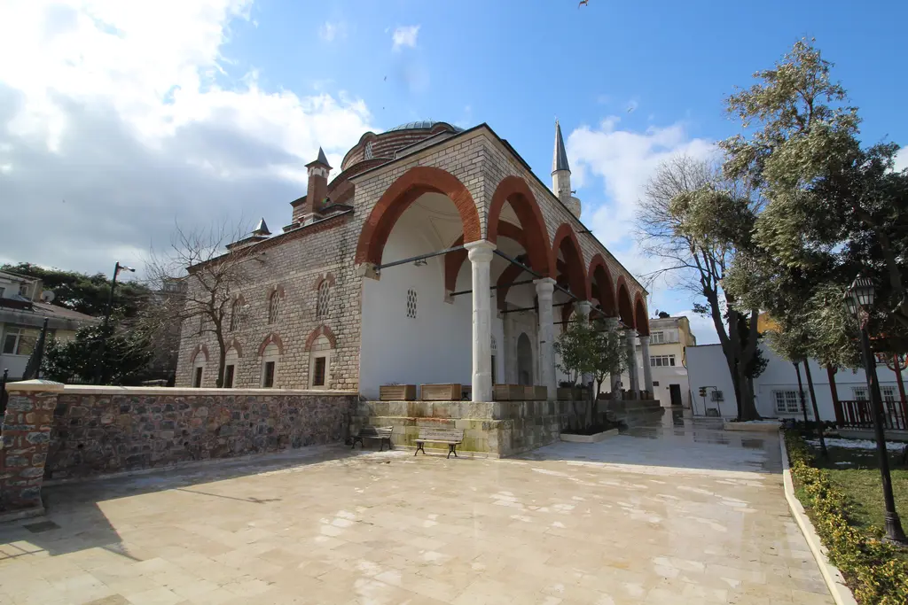 Rum Mehmed Paşa Camii'nin avlusu; kemerli revak, beyaz sütunlar, taş zemin ve arkada sıvalı cami duvarı.