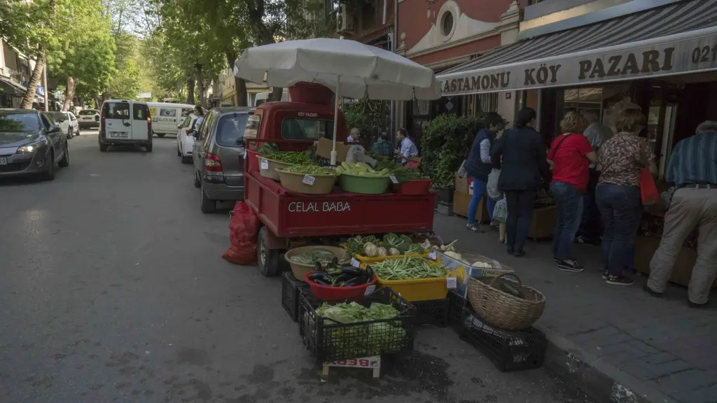 Kuzguncuk'ta İcadiye Caddesi; sebze tezgâhları, şemsiye altında satıcı, dükkân vitrinleri ve kaldırımda insanlar.