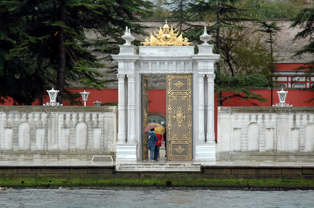 Beylerbeyi Sarayı'nın deniz kapısı; rıhtım duvarında beyaz mermer kapı, üstünde altın yaldızlı arma ve önünde ziyaretçiler.