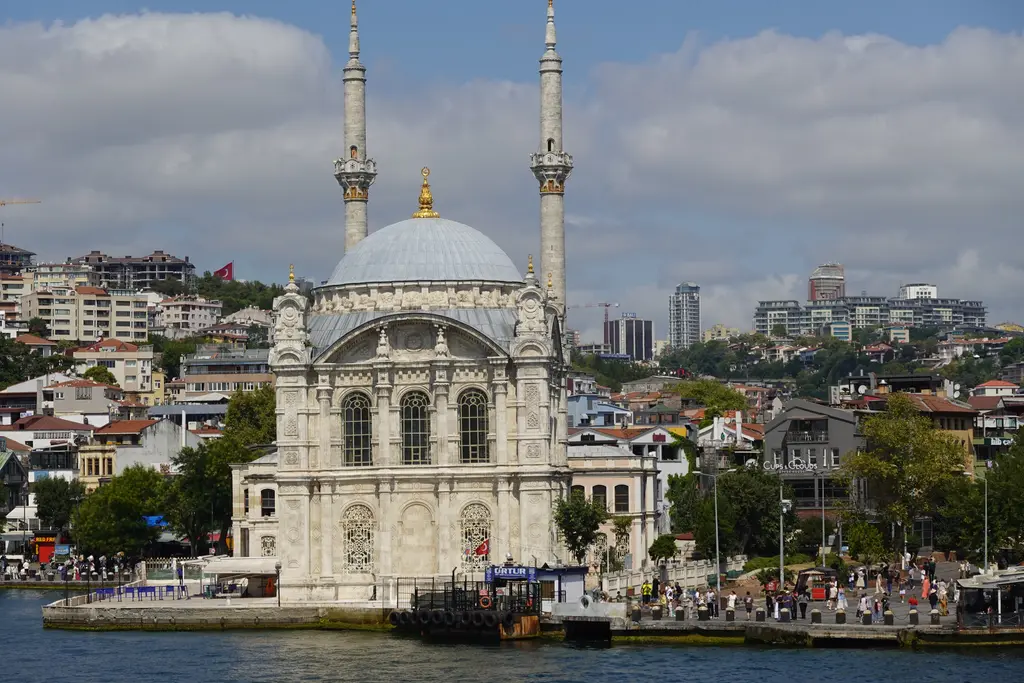 Ortaköy meydanından cami; önde kalabalık ve tezgâhlar, ortada beyaz cephe ve kubbe, iki yanda minareler.
