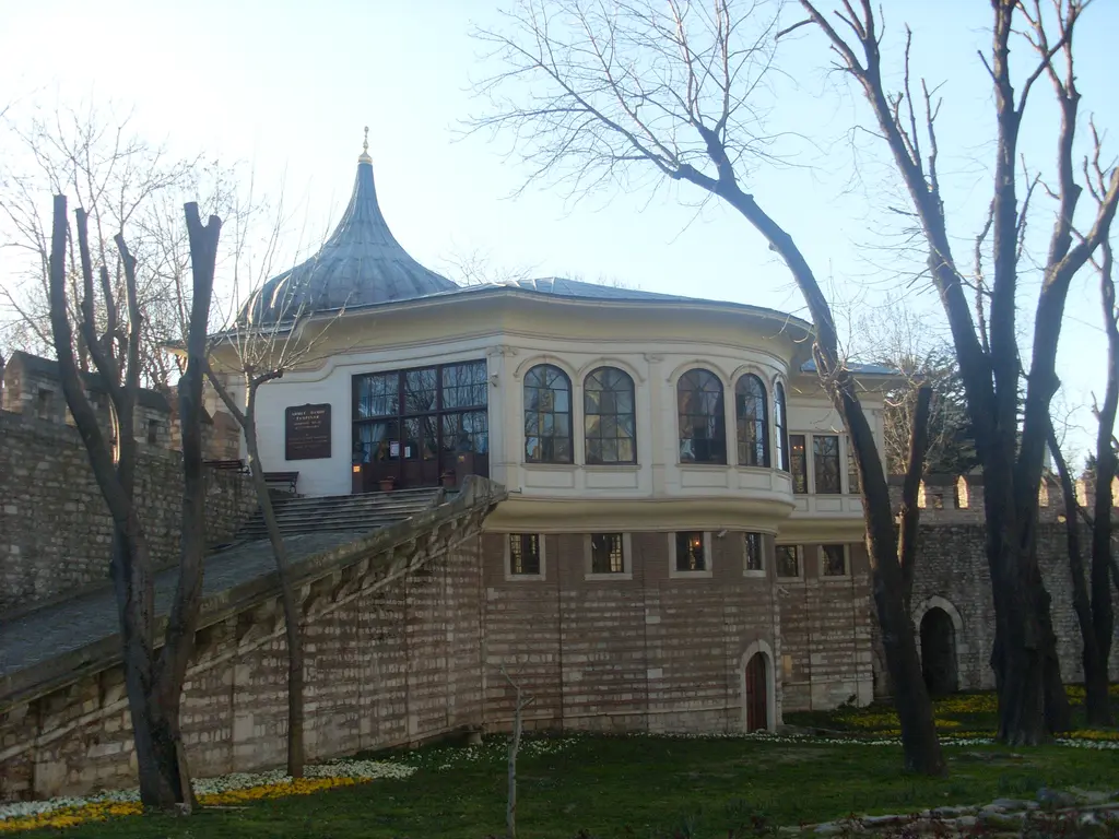 Gülhane Parkı tarafından Alay Köşkü; kurşun soğan kubbe, geniş pencereli yarım daire sofa, sur boyunca uzanan taş rampa ve yapraksız ağaçlar.
