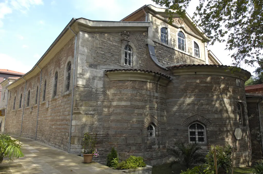 Aya Yorgi Kilisesi dıştan; kesme taş gövde, kiremit kaplı alçak çatı, yuvarlak apsis çıkıntısı ve çevresinde bahçe.