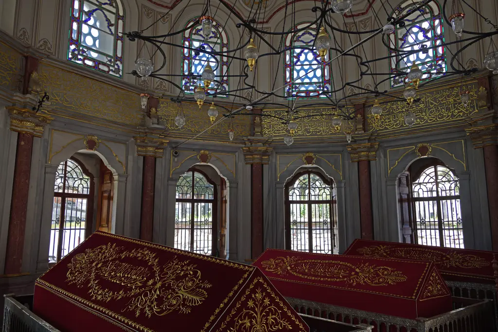 Mihrişah Valide Sultan Türbesi'nde sandukalar; kırmızı yaldız işlemeli örtüler, şebekeli pencereler, sütunlar ve renkli camlı üst pencereler.