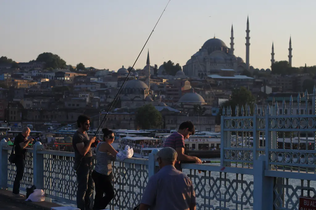 Akşamüstü köprüde balıkçılar; korkuluğa yaslanan insanlar, arkada tepede Süleymaniye Camii ve yamaçtaki binalar.