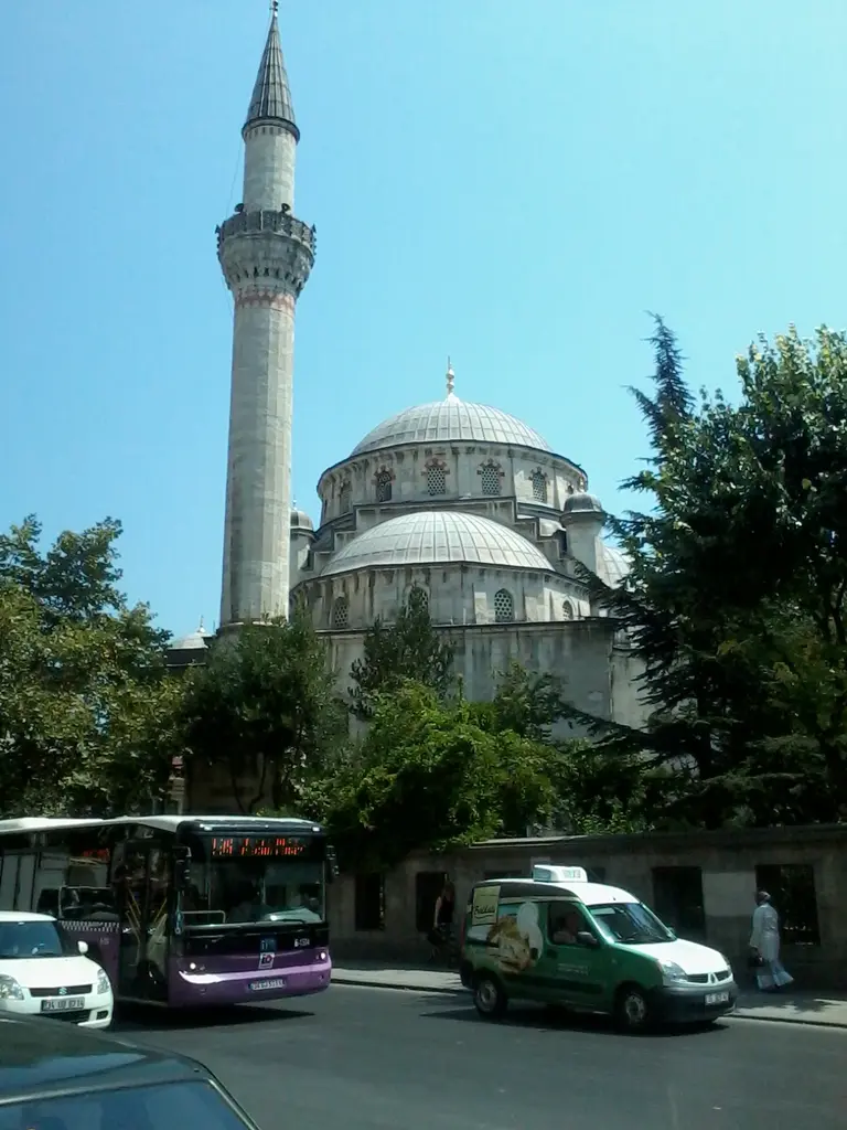 Şişli Camii'nin minaresi ve kubbesi; ince tek şerefeli minare, kurşun kaplı ana kubbe, ağaçlar ve önde caddedeki otobüs.