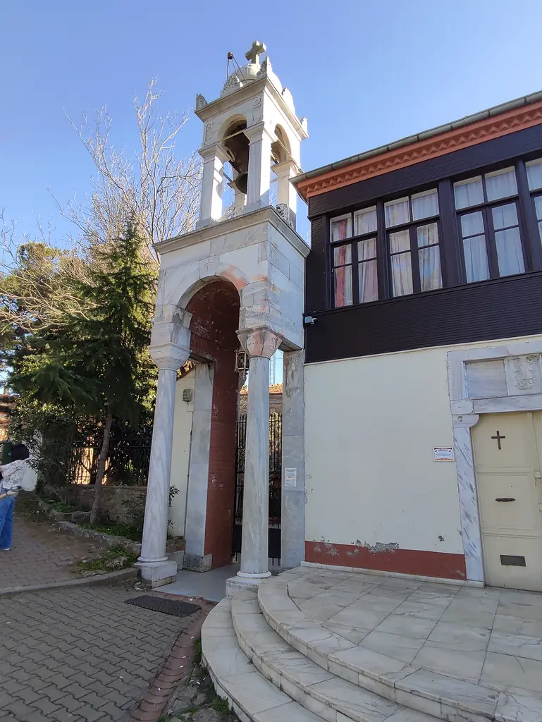 Aya Yorgi Manastırı'nın girişi; kemerli beyaz çan kulesi, kavisli mermer basamaklar ve ahşap çıkmalı bina.