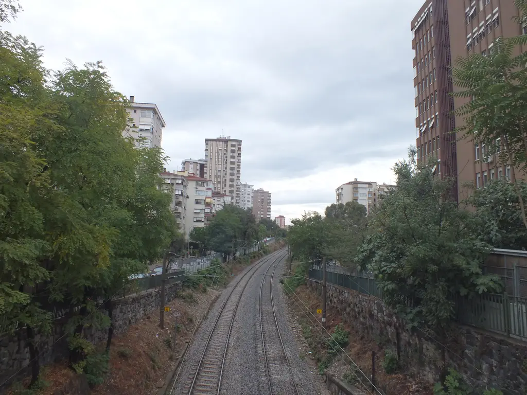 Göztepe'de demiryolu; köprüden doğuya bakış, iki yanı ağaçlı yarma içindeki raylar ve arkada apartmanlar.