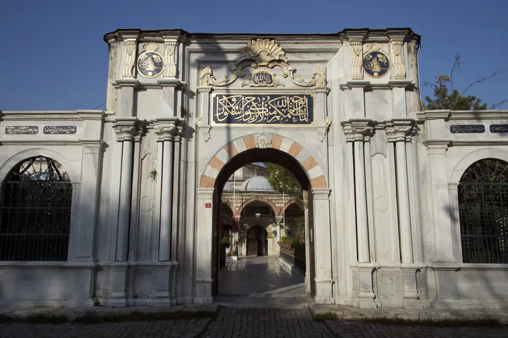 Mihrişah Valide Sultan İmareti'nin kapısı; pembe-beyaz mermer kemer, yaldızlı yazı panosu, tuğralı madalyonlar ve açık kapıdan görünen avlu.
