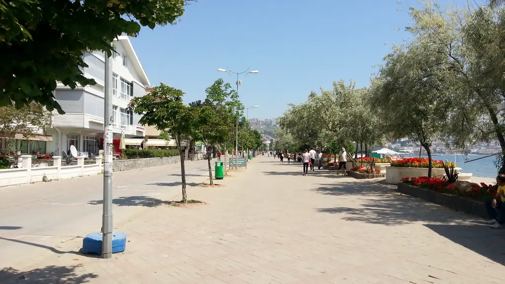 Büyükçekmece'de kordon; geniş taş döşeli yürüyüş yolu, ağaçlar, çiçek saksıları ve yürüyenler.