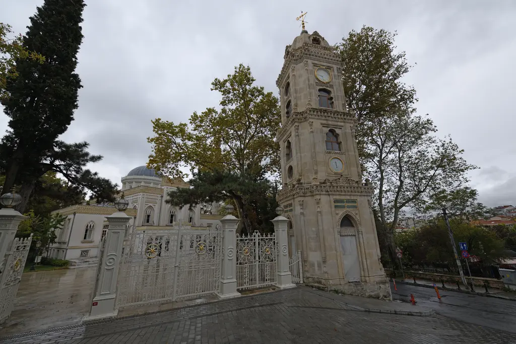 Yıldız saat kulesi ve avlu kapısı; üç katlı taş kule, beyaz demir kapı ve parmaklıklar, arkada kubbe ve ağaçlar.
