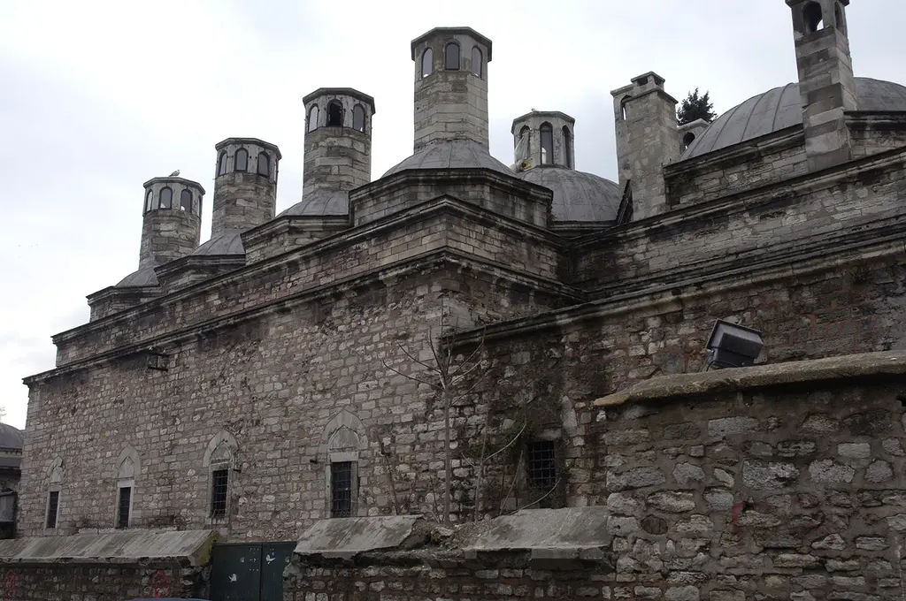 Haseki Sultan Külliyesi'nde kesme taş bir yapının üstünde sıralanan silindir bacalar, kurşun kubbeler ve bulutlu gök.