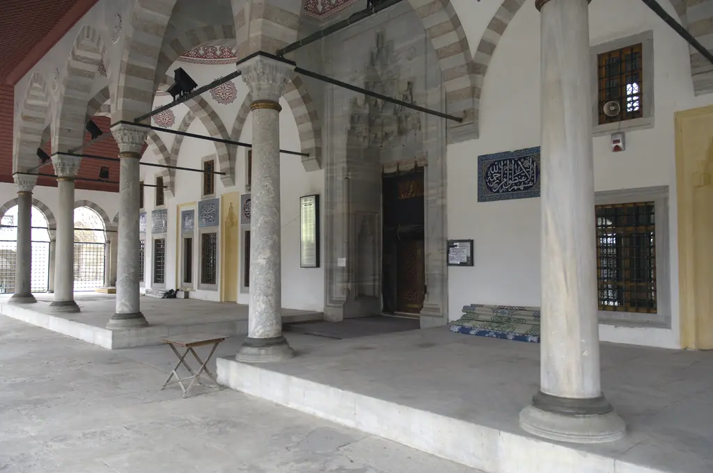Atik Valide Camii'nin revakı; mermer sütunlar, kırmızı ahşap tavan, taş zemin ve duvardaki çini levhalar.