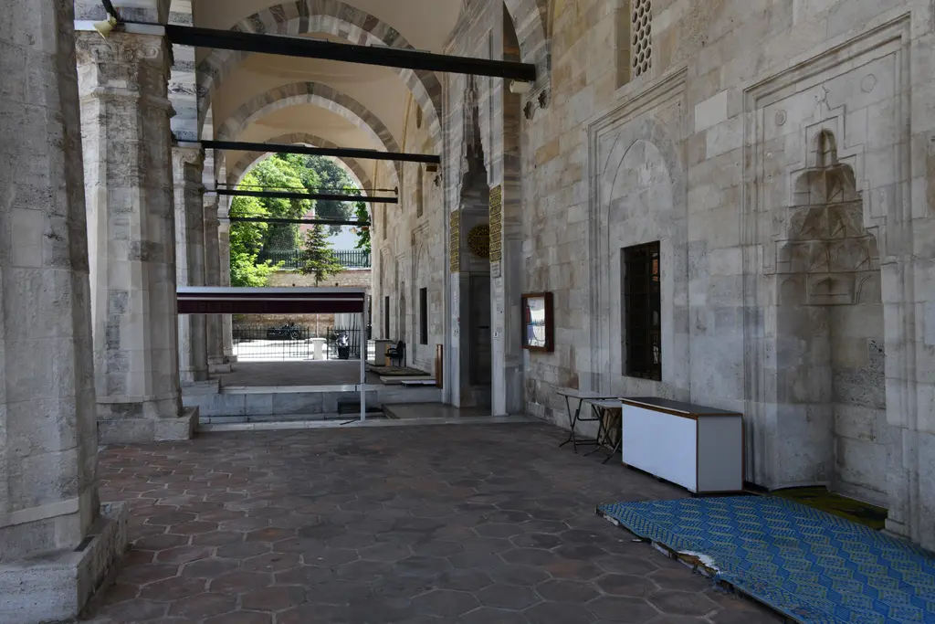 Mahmut Paşa Camii'nin son cemaat yeri içeriden; taş kemerler, altıgen döşeme, duvarda mukarnaslı niş, pencere ve zemindeki mavi seccade.
