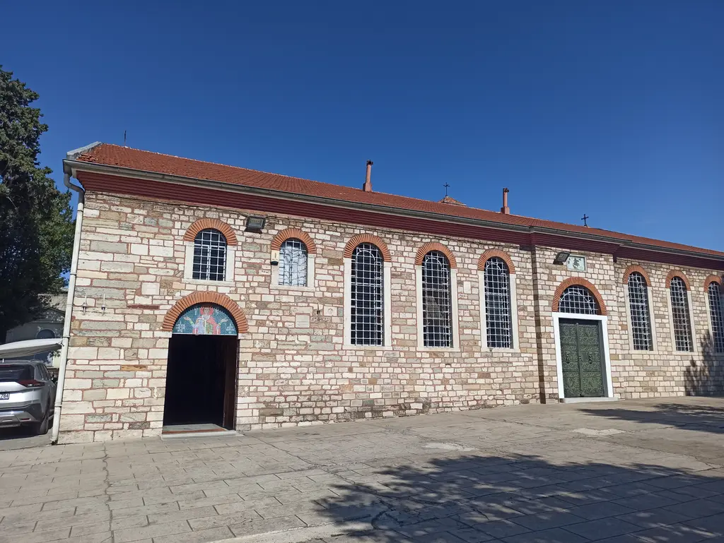 Kurtuluş'ta Aya Dimitri Rum Ortodoks Kilisesi; taş ve tuğla örgülü kemerli pencereli uzun cephe, kiremit çatı ve taş avlu.