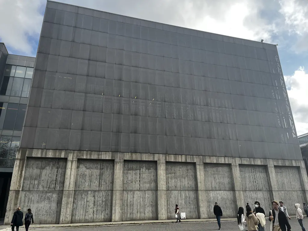 Santralistanbul'da sanat binası; dev gri kutu biçimli metal kaplı cephe, beton ayaklar ve önünde yürüyen ziyaretçiler.