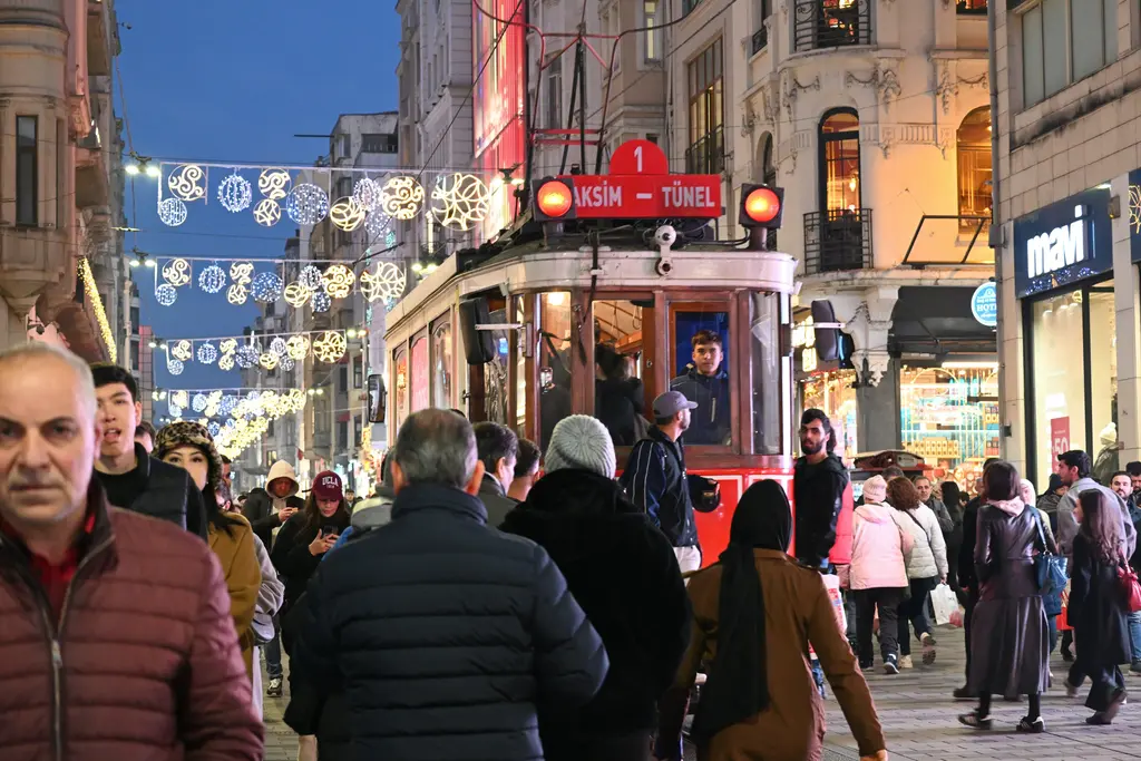 Beyoğlu'nda akşam İstiklal Caddesi; ışıklı süslemelerin altında ilerleyen kırmızı nostaljik tramvay, iki yanda vitrinler ve yoğun yaya kalabalığı.