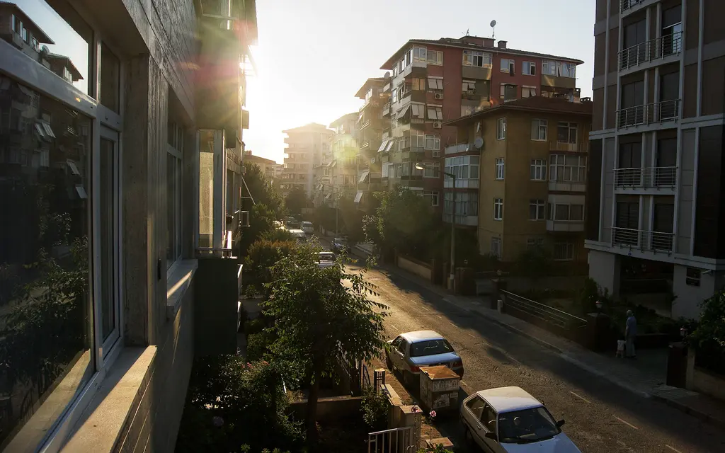 Göztepe'de bir sokak; balkondan bakış, ağaçlı yokuş, park etmiş arabalar ve gün ışığında apartman cepheleri.