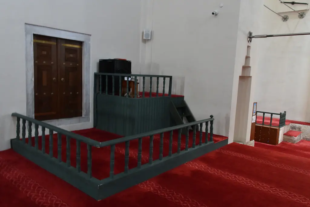 Mahmut Paşa Camii'nde müezzin mahfili; yeşil boyalı ahşap korkuluklu alçak platform, arkada ahşap kapı, sağda ince sütunlar ve kırmızı halı.