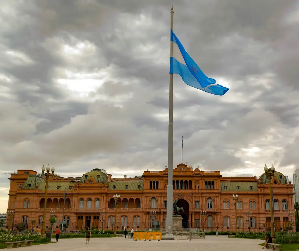 Buenos Aires'te Casa Rosada; pembe boyalı cephesi, yeşil kubbeleri, önündeki Plaza de Mayo ve dalgalanan Arjantin bayrağı.
