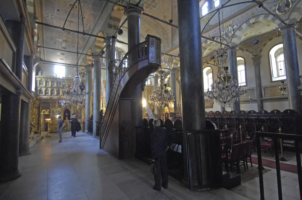 Aya Yorgi Kilisesi'nde koyu ahşap ambon; külahlı tepeliği, oymalı korkuluğu, yanında mermer sütun ve arkada yaldızlı ikonostasisin bir bölümü.