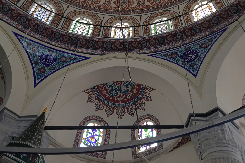 Azapkapı Sokullu Mehmed Paşa Camii'nde kubbe geçişi; çinili üçgen yüzeylerde yuvarlak yazı madalyonları, kalem işli yarım kubbe ve renkli pencereler.