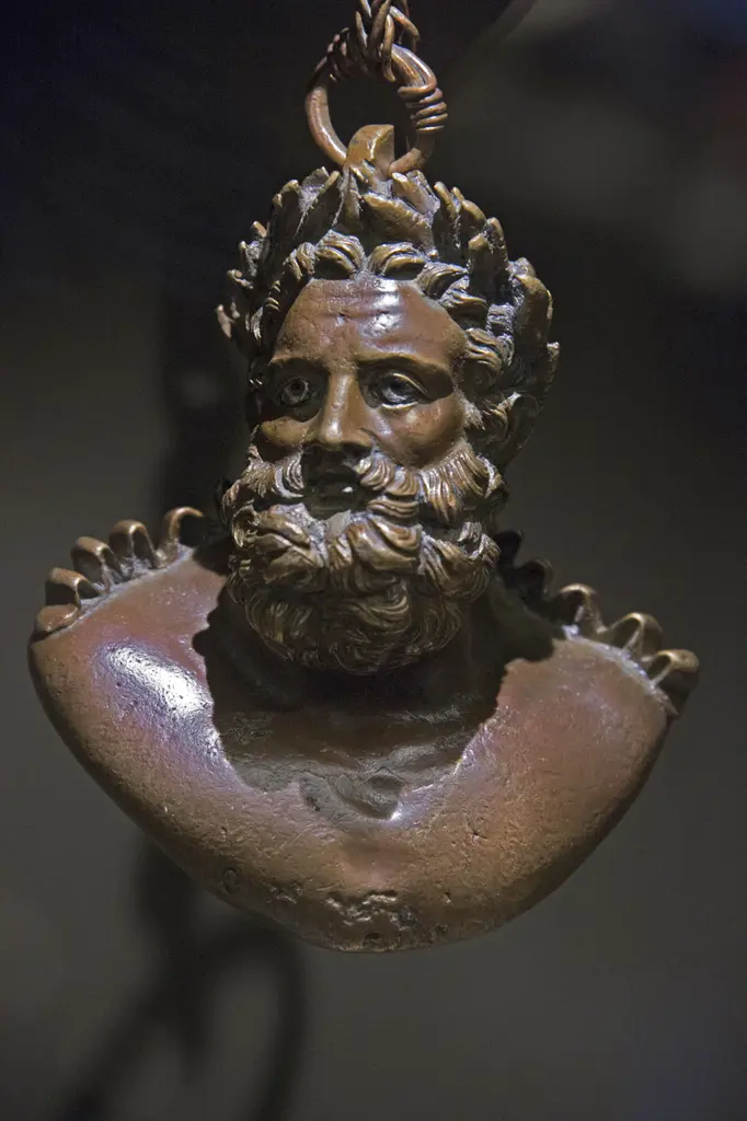 Karanlık fonda zincirle asılı, sakallı bir erkek büstü biçiminde bronz ağırlık.