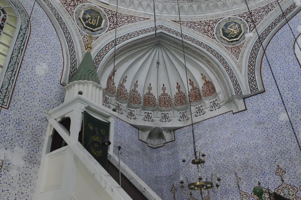 Haseki Sultan Camii'nin beyaz mermer minberi; yeşil külahlı köşk, arkada mukarnaslı yarım kubbe ve mavi kalem işi desenli duvar.