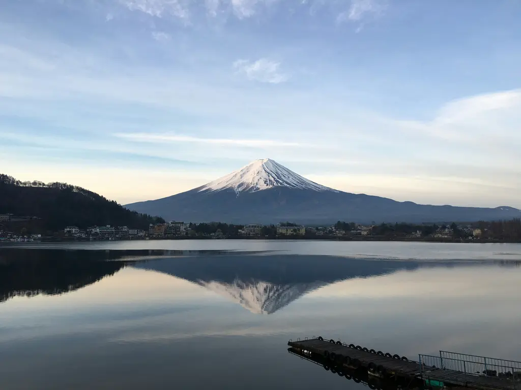 Japonya'da karlı zirvesiyle Fuji Dağı; önündeki durgun göle bütünüyle yansımış koni, kıyıda küçük bir kasaba ve iskele.