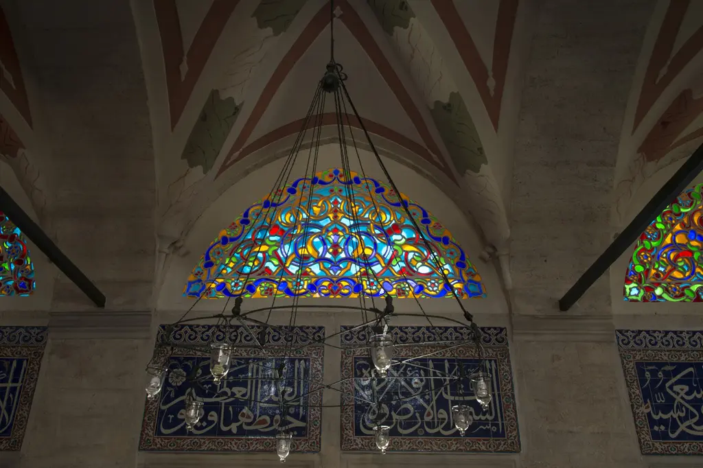 Kılıç Ali Paşa Camii'nde renkli camlı pencere; mavi, kırmızı ve sarı camlarla dolu yarım daire biçimli alçı pencere ve altında çini panolar.