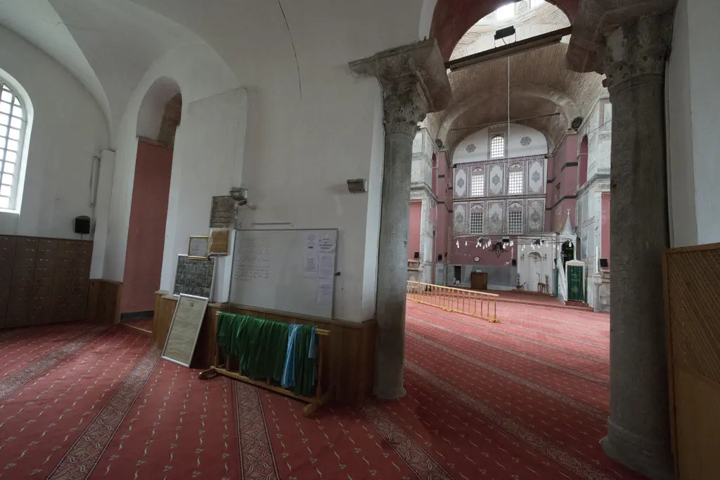 Kalenderhane Camii'nin iç narteksi; iki gri mermer sütunun arasından harime bakış, uzakta mihrap duvarı, önde kırmızı halı.